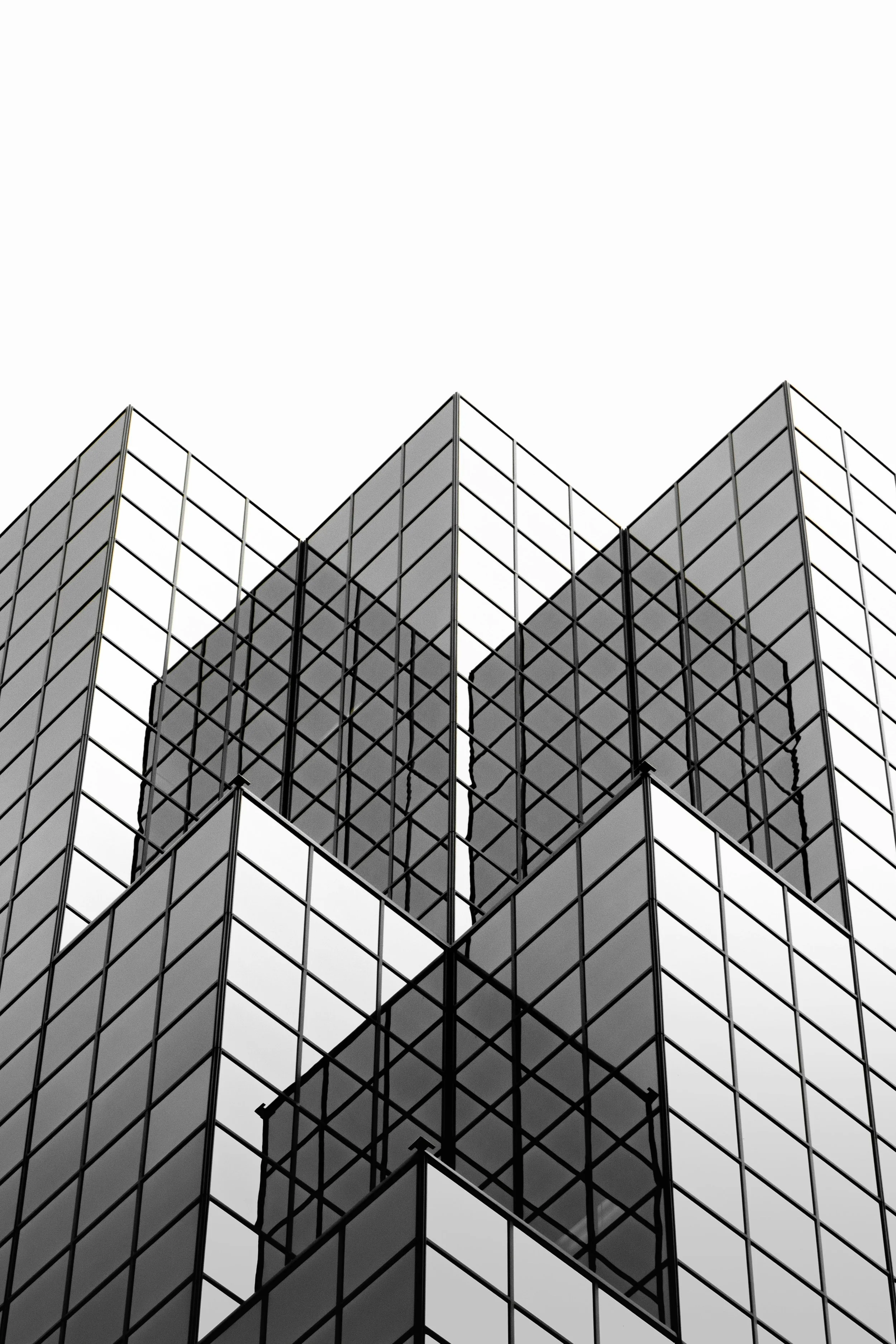 Black and white photograph of the glass exterior of a modern high-rise building with reflective windows forming geometric patterns.