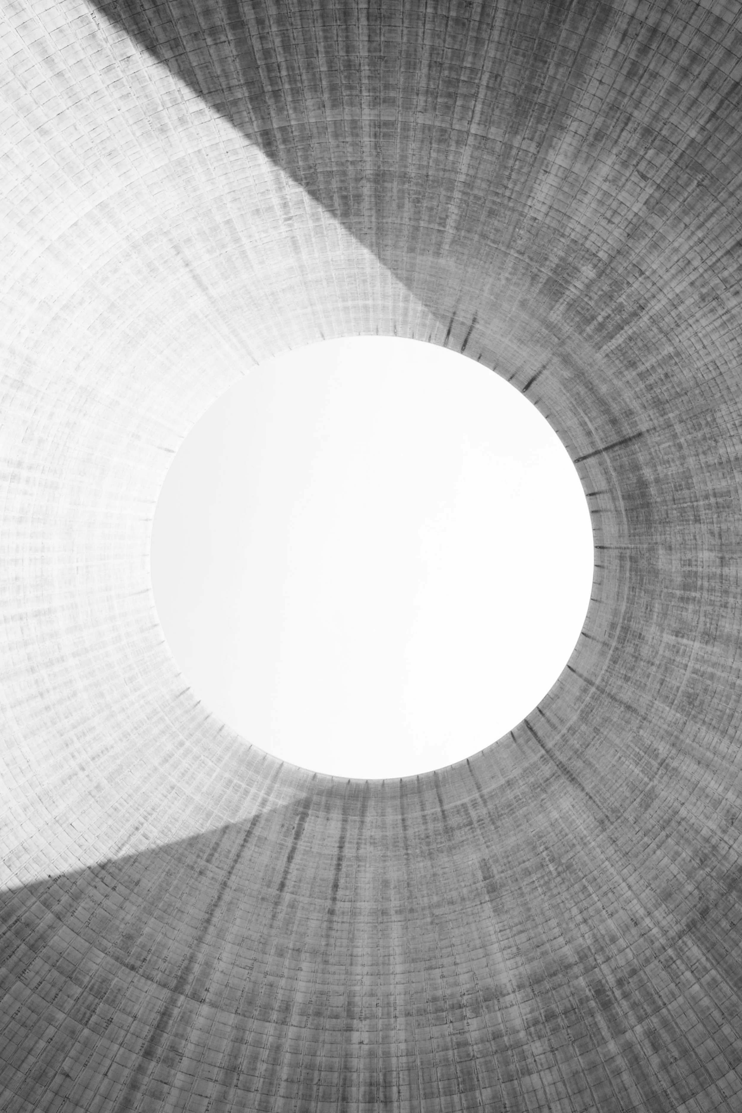 Looking up at the inside of a tall, cylindrical concrete cooling tower with a circular opening at the top