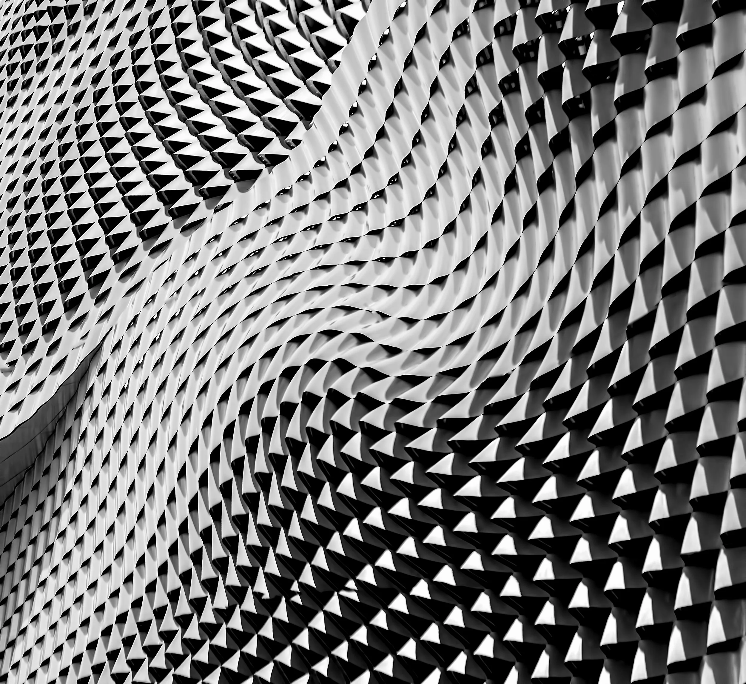 Black and white abstract building facade with a textured, geometric pattern of repetitive angular shapes.